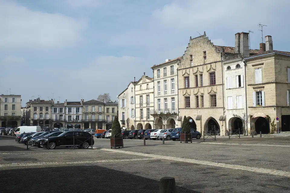 Place de la Cathédrale à Bazas, entourée de maisons anciennes à arcades et de façades en pierre aux toits de tuiles.